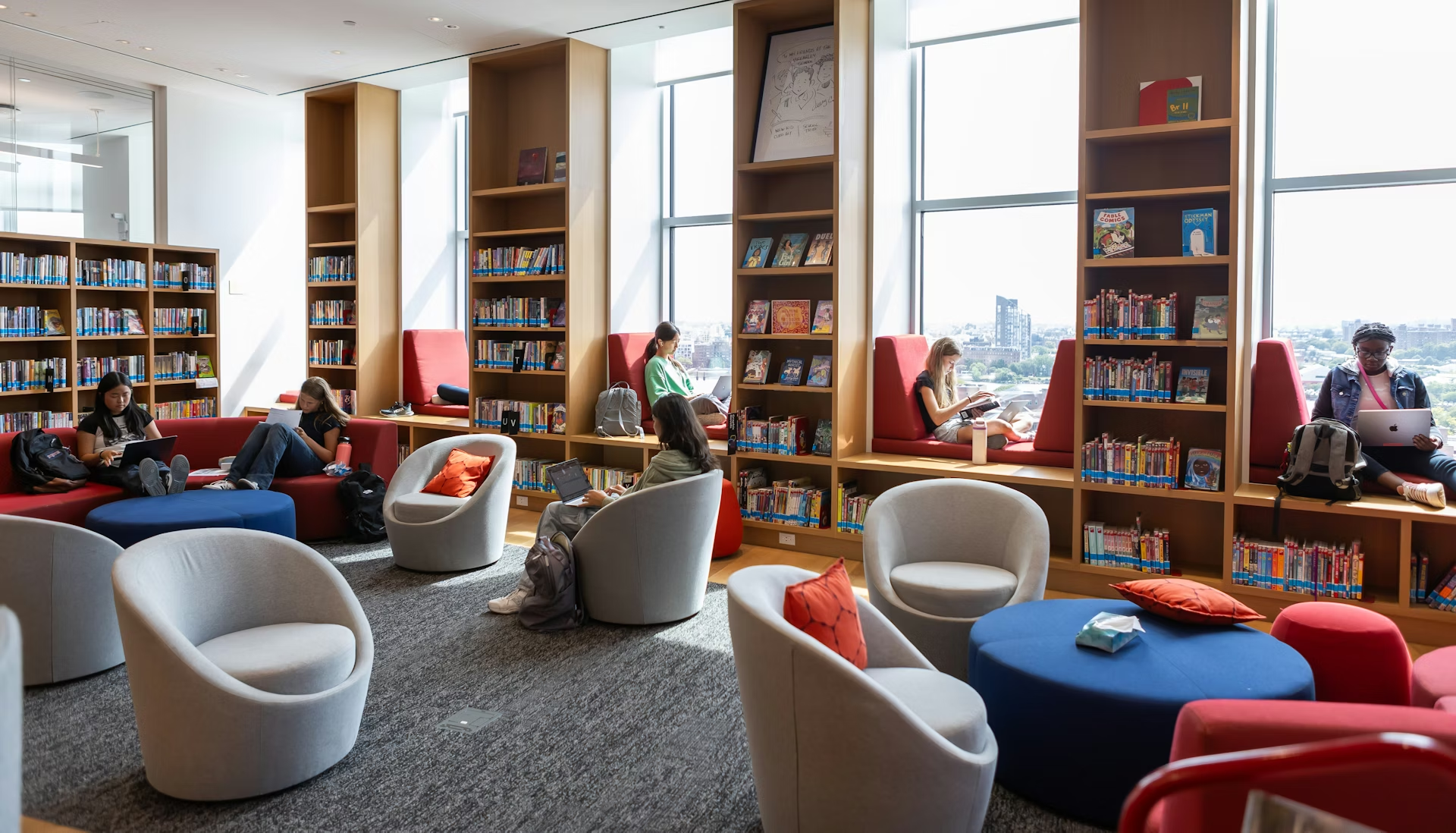 Ruang baca perpustakaan dengan rak buku dan tempat duduk di dekat jendela